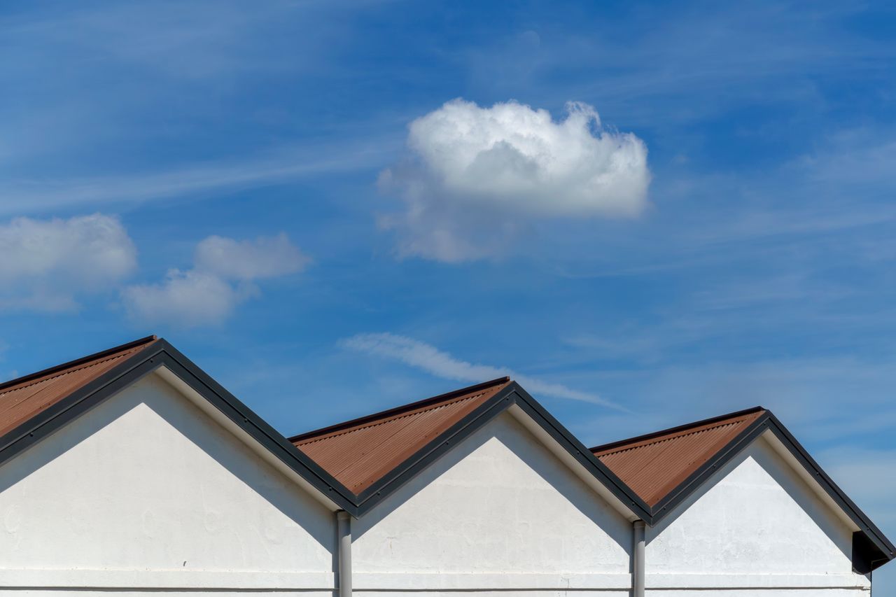 Gable roofs with sharp angles under a vibrant blue sky and soft clouds. Ideal for architectural studies.